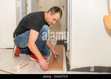 Uomo che lavora con le dita amputate. Sta lavorando alla posa del pavimento in casa sua durante il giorno. Foto Stock