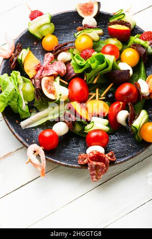Spuntino festivo di gamberetti, jamon, frutta e verdure su spiedini di legno. Foto Stock