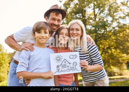 Famiglia felice con due bambini che tengono disegno che simboleggia la costruzione della casa e la proprietà della casa Foto Stock
