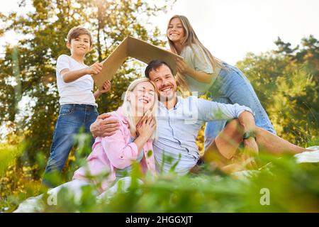 Genitori e bambini nel parco con un tetto sopra le loro teste come simbolo per la loro casa e la costruzione della casa Foto Stock