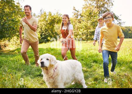 Famiglia felice con i bambini e il cane è in esecuzione su un prato verde in estate Foto Stock