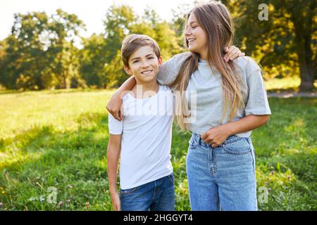 Fratello e sorella abbracciando felicemente nel parco verde durante le vacanze estive Foto Stock