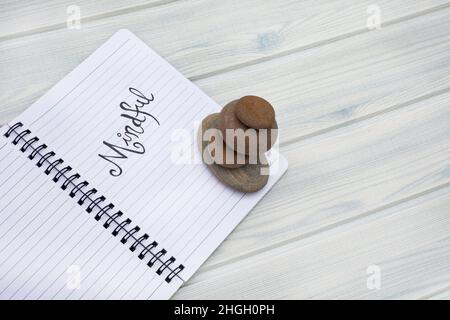 Taccuino con la parola mindful scritta su di esso. Posto su un colore pastello di legno con atmosfera da spiaggia Foto Stock