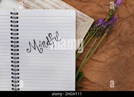 Taccuino con la parola mindful scritta su di esso. Posto su una superficie rustica Foto Stock