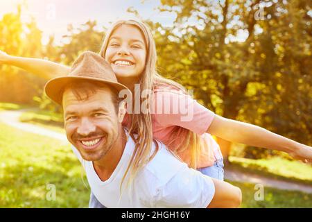 Felice padre porta la sua figlia ridente piggyback sulla sua schiena in estate Foto Stock