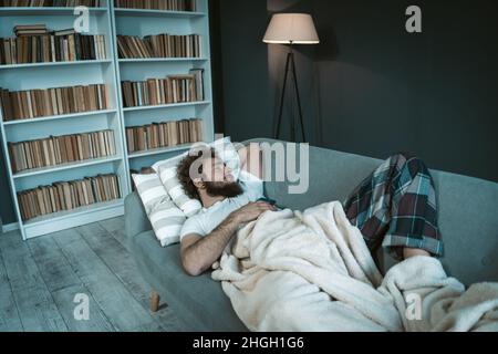 Il modello maschio dorme sul divano nel suo appartamento. Concetto di vita studentesca. Notte, comfort di casa, tempo di dormire. Foto di alta qualità Foto Stock