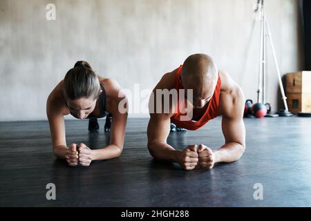 Spingi la tua strada verso il fitness. Shot di un uomo e di una donna che fanno esercizi di asse in palestra. Foto Stock