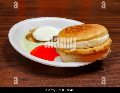 Sauth asiatico cibo pollo bun kabab con salsa di pomodoro e piccante Chutney in piatto bianco isolato su tavola di legno scuro famoso pakistano, indiano, Banglade Foto Stock