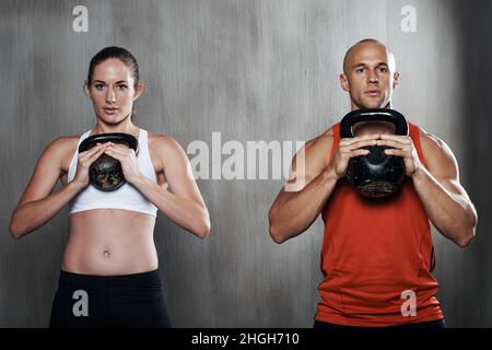 Si impegnano a mantenere la forma. Un uomo e una donna che si allenano con le campane del bollitore in palestra. Foto Stock