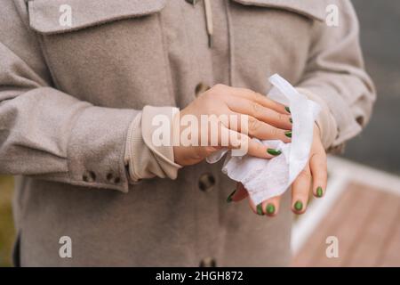 Primo piano scatto ritagliato di donna irriconoscibile utilizzando salviette antibatteriche bagnate per pulire e disinfettare le mani all'aperto. Foto Stock