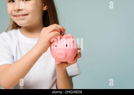 Una bambina mette una moneta in una banca piggy. Il concetto di insegnare ai bambini la finanza personale e il risparmio Foto Stock