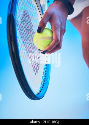 Il suo gioco di servizio è sul punto. Scatto corto di una giovane giocatore di tennis femminile irriconoscibile che si prepara a servire su sfondo blu. Foto Stock