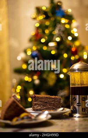 Pezzo di torta sul piatto con tazza di caffè e albero di natale sfocato sullo sfondo. Foto Stock