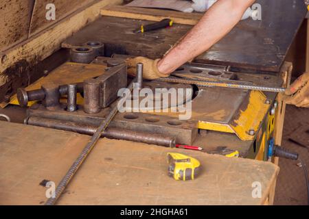 Montaggio di barre di rinforzo per la colata di calcestruzzo. Background industriale. L'operatore sta piegando le barre di armatura con la macchina piegatrice di armatura nel luogo. Foto Stock