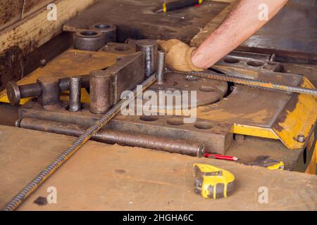 Montaggio di barre di rinforzo per la colata di calcestruzzo. Background industriale. L'operatore sta piegando le barre di armatura con la macchina piegatrice di armatura nel luogo. Foto Stock