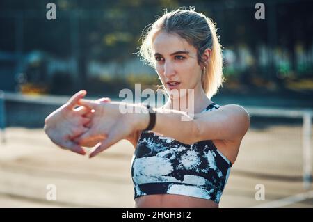 Preparazione con alcuni tratti. Scatto di una giovane donna sportiva che allunga le braccia mentre si esercita su un campo da tennis. Foto Stock
