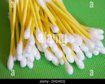 Un gran numero di tamponi di cotone su sfondo verde, un primo piano. Tamponi di cotone o bugne di cotone. Sono più comunemente utilizzati per la pulizia delle orecchie. Foto Stock