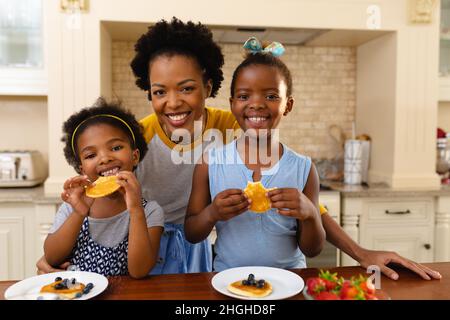 Ritratto della madre afroamericana e delle sue due figlie che hanno fatto colazione in cucina a casa Foto Stock