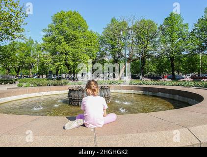 Bambina seduta vicino alla fontana nel parco primaverile Foto Stock