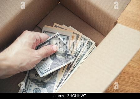 Un uomo che mette le fatture del dollaro in una scatola di cartone. Primo piano. Foto Stock