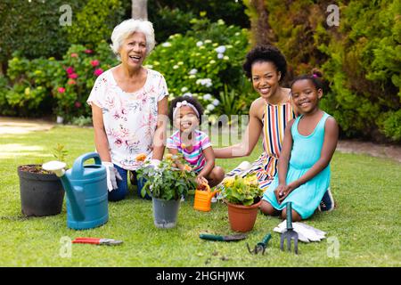 Ritratto di sorridente tre famiglia generazionale giardinaggio femminile insieme a cortile Foto Stock