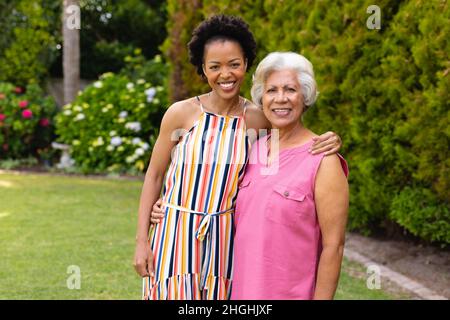 Ritratto di allegra donna afroamericana in piedi con braccio intorno a madre anziana in cortile Foto Stock