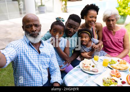 Ritratto di tre famiglie afroamericane generazionali che prendono selfie seduti al tavolo da pranzo Foto Stock