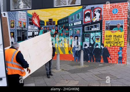 Due uomini trasportano forniture da un furgone bianco e passato un murale che ricorda le rivolte di Brixton 1981 e il razzismo sistematico e le molestie da parte della polizia della comunità nera di Brixton, il 21st gennaio 2022, a Railton Road, Londra, Inghilterra. L'opera, realizzata dagli artisti Jacob V Joyce, Monique Jackson, Ailsa Yexley, Buki Bayode e sola Olulode, è stata coronata da fondi e rappresenta il 40th° anniversario delle rivolte di Brixton del 1981, quando il radicamento è iniziato dal 10th, 11th e 12th aprile 1981 su Brixton's Railton Road, nota come Front Line .. (Didascalia completa in informazioni aggiuntive). Foto Stock