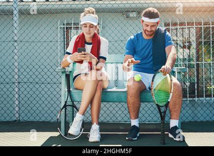 È il momento di rilassarsi un po'. Scatto completo di due giovani giocatori di tennis seduti e conversando in campo. Foto Stock