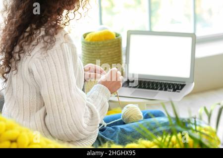 Giovane donna afroamericana che prende le classi di maglieria in linea nel paese Foto Stock