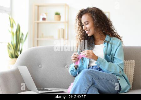 Giovane donna afroamericana che prende le classi di maglieria in linea nel paese Foto Stock