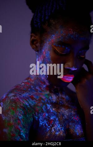 ritratto di giovane donna nera con coloratissimo make-up astratto sul viso. scatto insolito, interessante, fantastico. body art, luci al neon, fluorescenza. clos Foto Stock