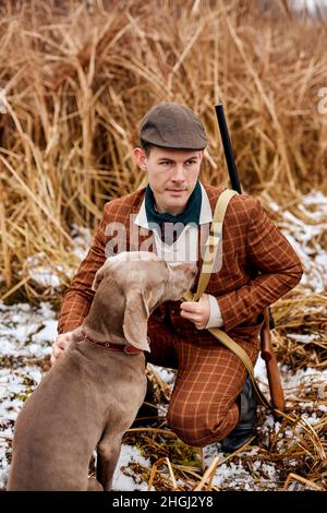 giovane americano caucasico bracconiere o cacciatore in cappello con pistola e weimaraner cane razza amico in campagna natura. Incredibile mattina d'autunno. Animali e. Foto Stock