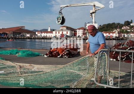 Pescatore locale che ripara le sue reti da pesca sulla banchina del porto di St Jean de Luz, Pays Basque, Nouvelle Aquitaine Foto Stock