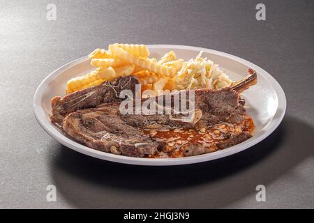 Salsa di agnello grigliato biologico con patatine fritte e insalata in piatto bianco su sfondo grigio scuro vista dall'alto Foto Stock