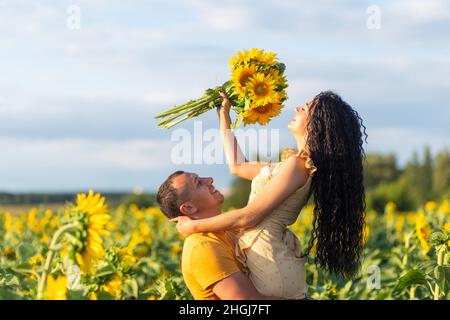 Una bella coppia giovane un uomo e una donna, abbracciano un campo di girasoli al tramonto. Il concetto di una vacanza estiva in famiglia, una romantica foto shoo Foto Stock