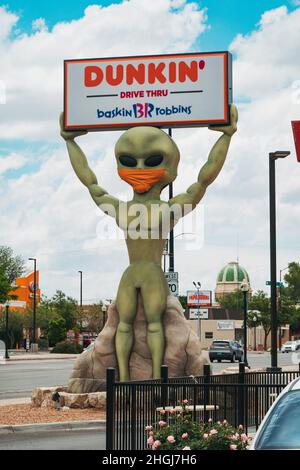 Una statua aliena custodisce un cartello Dunkin' Donuts a Roswell, New Mexico, mentre indossa una copertura facciale come simbolo di Covid-19 e maschere Foto Stock