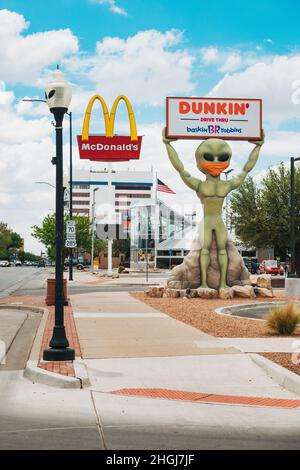 Una statua aliena tiene in mano un cartello Dunkin' Donuts a Roswell, New Mexico, mentre indossa una copertura facciale. Il ristorante McDonalds UFO è visibile dietro Foto Stock