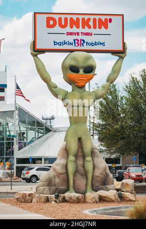 Una statua aliena custodisce un cartello Dunkin' Donuts a Roswell, New Mexico, mentre indossa una copertura facciale come simbolo di Covid-19 e maschere Foto Stock