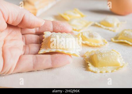 Donna mano che prepara la pasta ravioli. Primo piano su sfondo chiaro Foto Stock