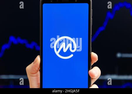 Ucraina, Odessa - Ottobre, 9 2021: Tenere a mano mobile con l'app CoinMarketCap in esecuzione sullo schermo dello smartphone, trading candelabro grafico in background. L'autorità di crittografia dei dati più affidabile al mondo Foto Stock