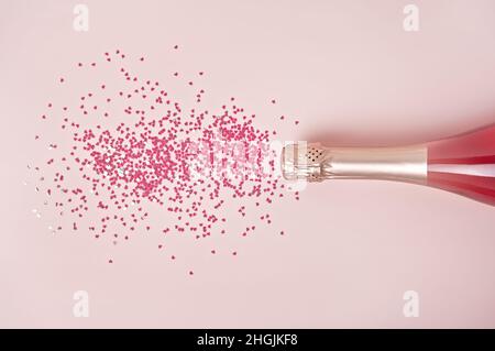 Design piatto alla moda e creativo con confetti rosa a forma di cuore versati da bottiglia di champagne su sfondo pastello. Disposizione piatta, vista dall'alto, spazio di copia. Biglietto di auguri per buon San Valentino. Foto Stock