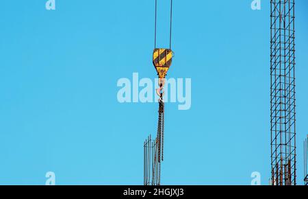 Ganci appesi alle grandi catene della gru discendenti dall'alto. Sfondo blu cielo. Foto Stock