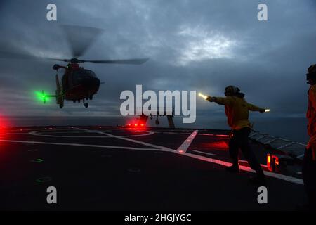 ENS. Ryan Dunkle, membro dell'equipaggio della Guardia Costiera Cutter Healy (WAGB 20), trasmette i segnali di atterraggio ai piloti di Air Station Kodiak che volano su un elicottero MH-65 Dolphin durante le operazioni di addestramento notturno al largo della costa dell'Alaska durante lo spiegamento artico di Healy il 25 agosto 2021. Gli addetti al segnale di atterraggio sono responsabili della comunicazione con l'equipaggio e i membri dell'equipaggio di taglio durante le operazioni di volo. Foto Stock