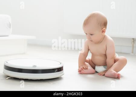 piccolo bimbo che gioca con l'aspirapolvere robot a casa. Felice famiglia che si sposta in un nuovo appartamento Foto Stock