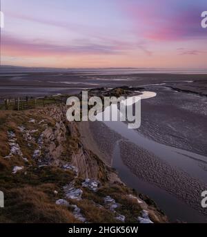 Una costa rocciosa che si dirige verso il mare e una spiaggia di sabbia al tramonto e un cielo rosa e viola Foto Stock