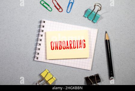 Simbolo di onboarding. Nota bianca con una parola 'onboarding' su bel tavolo di legno, carta colorata, matite colorate, graffette, monete e calcolatrice. B Foto Stock