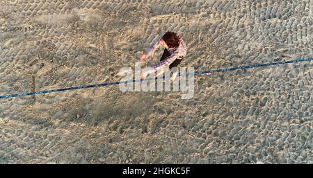 Vista aerea sopra il maschio slackliner bilanciamento su corda e fare acrobazie, dimostrando agilità, Pacific Beach a San Diego, California, Stati Uniti Foto Stock