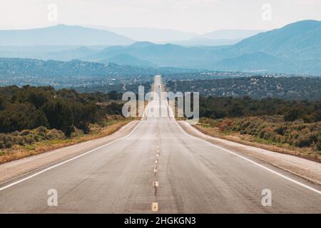 Un'autostrada si estende dritto su colline ondulate in lontananza alla periferia di Taos, New Mexico, Stati Uniti Foto Stock