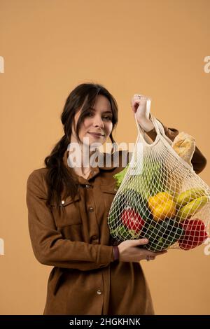 Donna che mostra una borsa riutilizzabile in mesh pieno di generi alimentari freschi. Zero sprechi. Pacchetti ecologici ed ecologici. Tela e lino fa Foto Stock